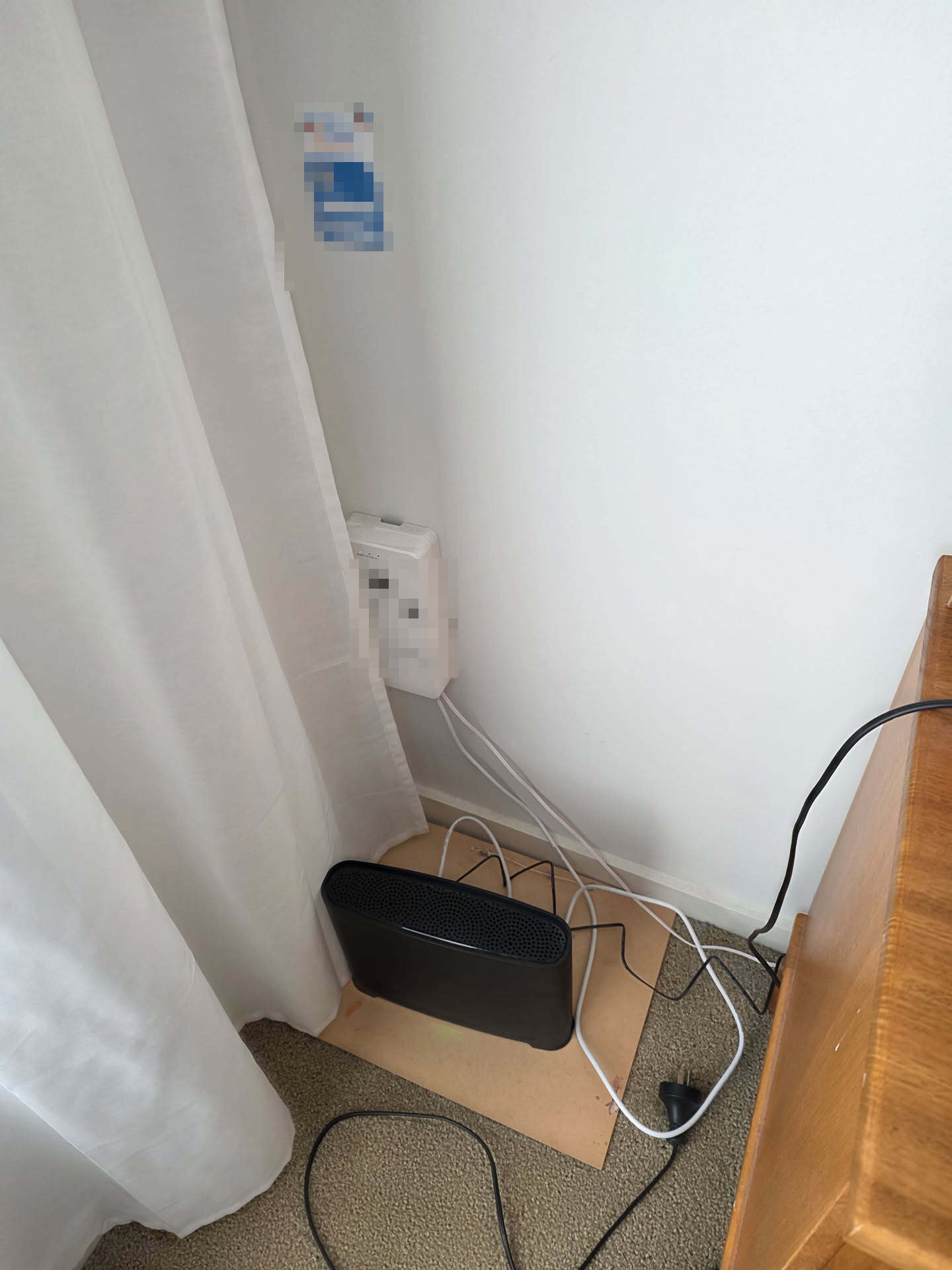 An NBN connection box in the corner of a bedroom with the modem left on the floor and cables running across the carpet