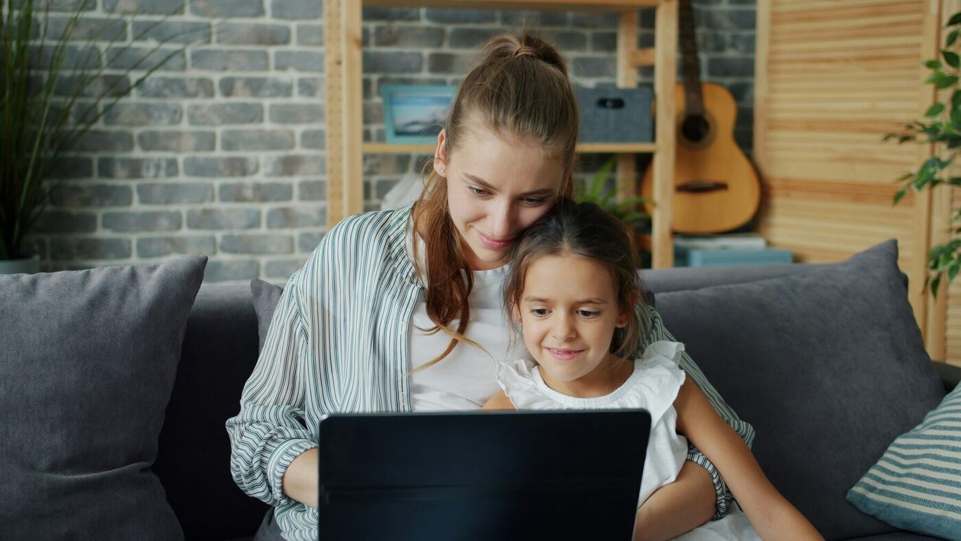 A mother and young daughter looking at a laptop screen together