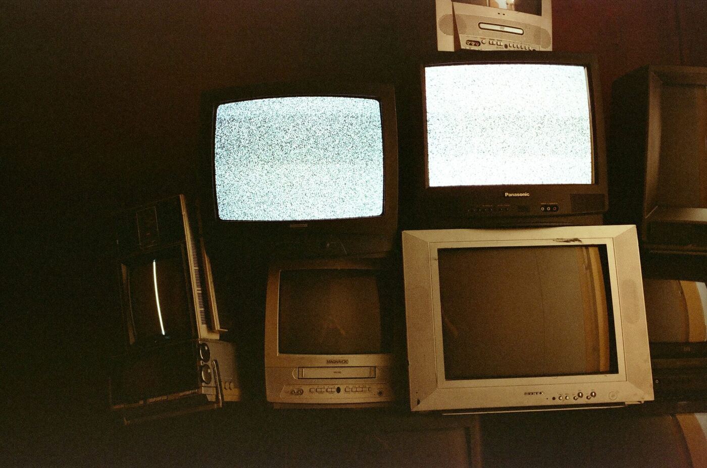 A stack of old televisions displaying static, evoking the cable TV era