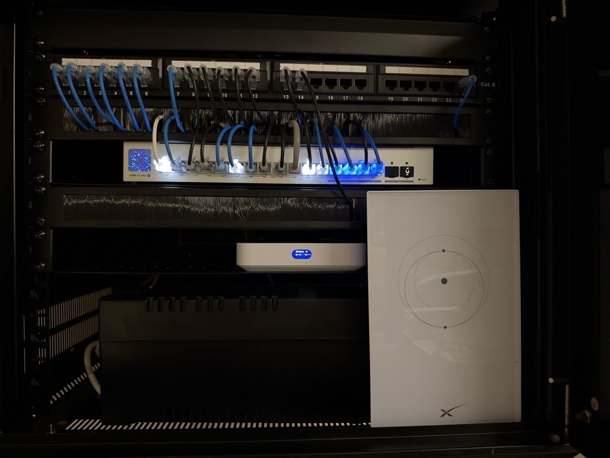 The finished cabinet seen front on: numbered ports along the top, one switch with its lights on, a small white gateway and the white Starlink unit