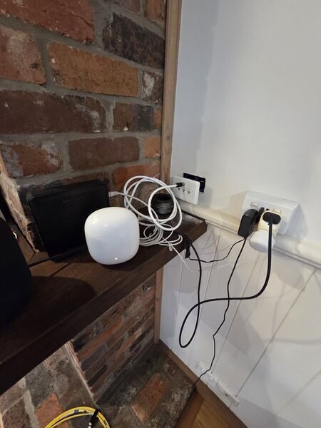 A modem and a mesh access point sharing a shelf against an exposed brick wall, with a coiled ethernet cable beside them