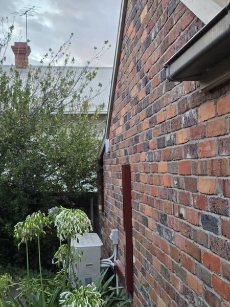 A utility enclosure mounted on the brick side wall of a house, where the incoming service reaches the building
