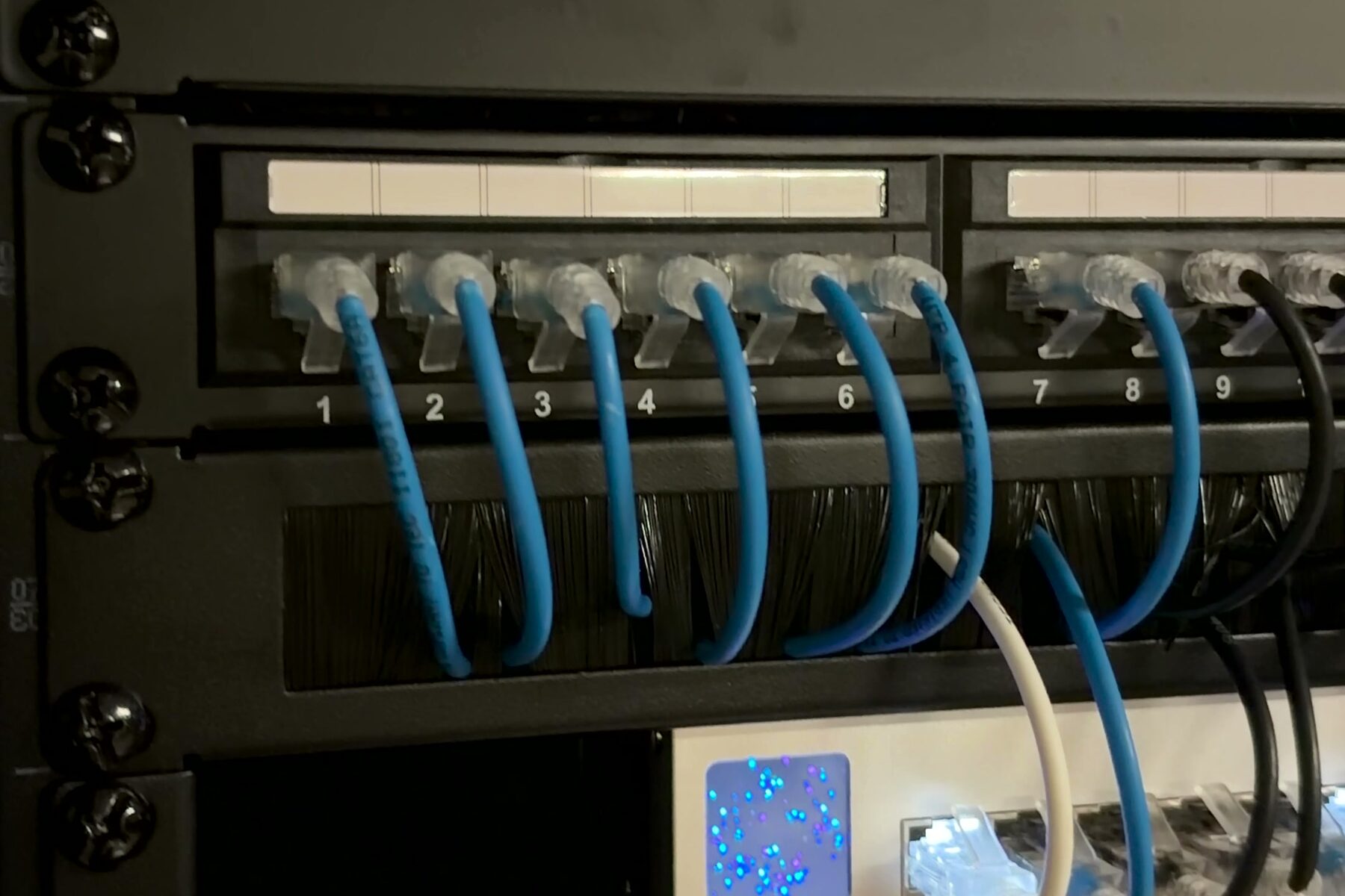 Short blue patch leads running from a numbered patch panel down to a network switch inside a cabinet